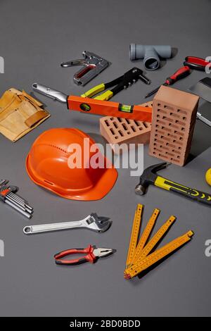 vue en grand angle de la ceinture porte-outils, des briques, des outils industriels et du casque orange sur fond gris Banque D'Images