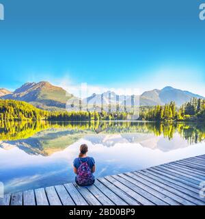 Belle jeune fille assise près d'un lac clair sous de merveilleuses montagnes dans les Hautes Tatras - Slovaquie. Lumière du matin sur le lac Strbske pleso. Photo avant Banque D'Images