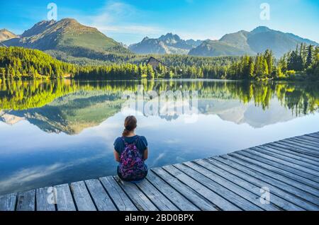 Belle jeune fille assise près d'un lac clair sous de merveilleuses montagnes dans les Hautes Tatras - Slovaquie. Lumière du matin sur le lac Strbske pleso. Photo avant Banque D'Images