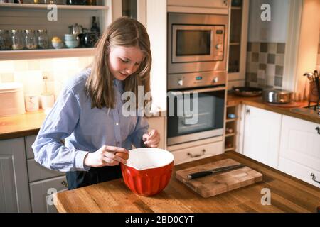 Une adolescente cuisiniers à la maison dans la cuisine brisant un oeuf dans un bol Banque D'Images