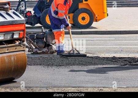 Un travailleur routier répare une partie de la route avec une patinoire, un rammer, un bulldozer et un niveau de bois. Banque D'Images