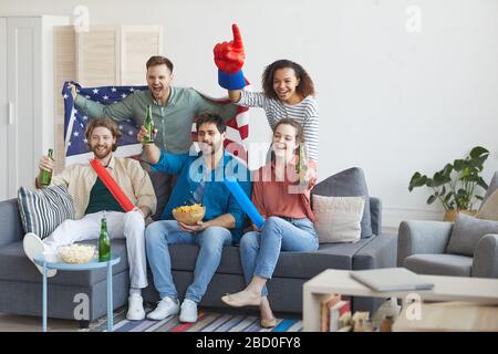 Portrait complet d'un groupe multi-ethnique d'amis regardant un match sportif à la télévision et encourageant émotionnellement tout en tenant le drapeau américain, copier l'espace Banque D'Images