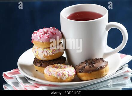 Tasse à thé blanche avec beignets sur une plaque blanche isolée sur fond bleu. Banque D'Images