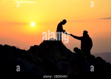 Deux amis s'aident les uns les autres et avec le travail d'équipe essayant d'atteindre le sommet de la montagne pendant le merveilleux lever du soleil d'été. Banque D'Images