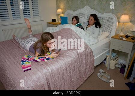 Détente en famille dans un lit lecture d'un livre et regarder iPad et téléphone Banque D'Images