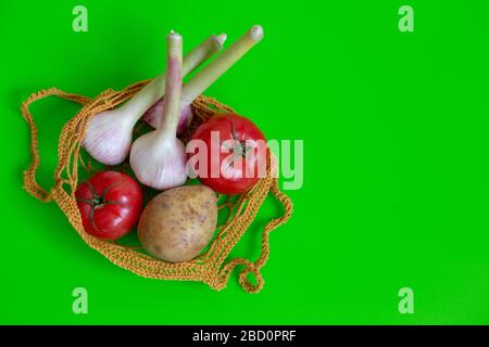 Sac tricoté sur une table verte avec légumes : tomates, ail, pommes de terre. Légumes végétariens. Alimentation saine. Vue de dessus. Espace de copie Banque D'Images