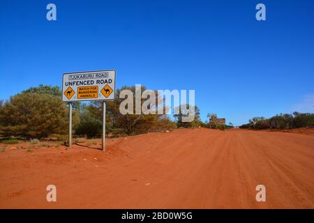 Vue grand angle de la route de la poussière rouge vers l'Australie occidentale avec panneaux routiers avertissant des chameaux se promenant autour ; territoire du Nord, Australie Banque D'Images