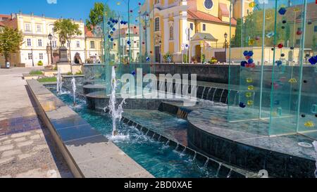 Gyor Hongrie 06 30 2019: Jeune femme regardant la fontaine à la place de la porte de Vienne dans l'arrière-plan de l'église de Carmélite. Banque D'Images