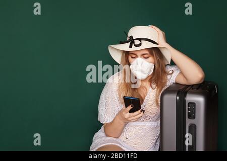 Les filles touristiques dans un masque médical se trouvent avec des bagages, téléphone dans les mains, sur un fond vert. COVID-19 éclosion de coronavirus. Concept de voyage Banque D'Images