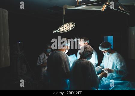 Une équipe professionnelle internationale de chirurgien, d'assistants et d'anesthésiste effectue une opération complexe sur un patient sous anesthésie générale. Sombre Banque D'Images
