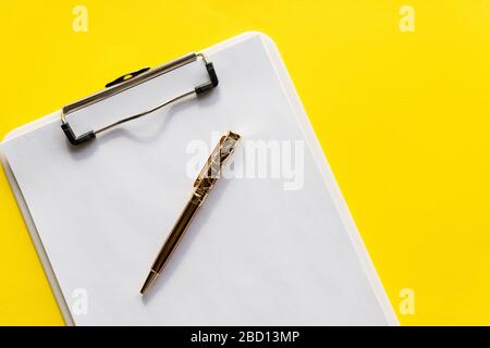 Presse-papiers avec papier vierge. Presse-papiers noir avec papier blanc vierge sur lequel est placé le stylo, sur fond jaune.espace de copie pour le texte. Design minimaliste Banque D'Images