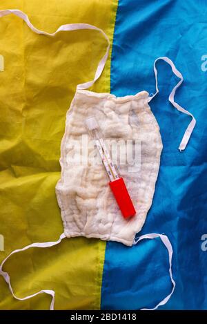 Masques de protection et thermomètre de gaze réutilisables sur fond bleu-jaune. Vue de dessus. La propagation du virus en Ukraine Banque D'Images