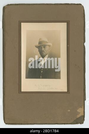 Photo d'un homme. Photo en noir et blanc d'un homme. Portant un costume sombre et une chemise claire, une moustache et une fédora de couleur claire, il se laque tout droit, légèrement à gauche du spectateur. Une étoile à l'intérieur d'un cercle, peut-être un symbole masonique, est partiellement visible sous son manteau ouvert. Photo d'un homme Banque D'Images