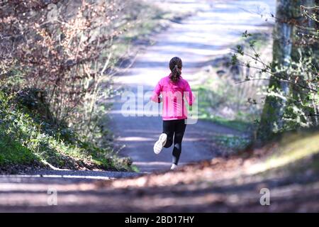 06 avril 2020, Bade-Wuerttemberg, Ravensburg: Une femme fait du jogging le long d'un sentier forestier près d'une réserve de jeux. Des dizaines de personnes sont attirées pour marcher et courir dans la forêt au-dessus du Schussental. Photo: Felix Kästle/dpa Banque D'Images