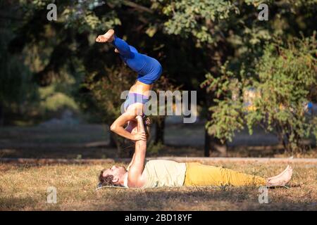 Jeune couple faisant des exercices d'acroyoga dans le parc. Homme tenant la femme sur les mains dans les poses acro yoga Banque D'Images