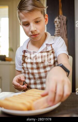 Garçon en tablier déballage des biscuits savoiardi préparer le dessert tiramisu. Restez à la maison et faites cuire les aliments de fond Banque D'Images