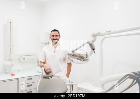 Portrait d'un dentiste barbu homme portant un uniforme blanc, debout dans une clinique de dentiste. Banque D'Images