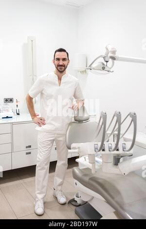 Portrait d'un dentiste barbu homme portant un uniforme blanc, debout dans une clinique de dentiste. Banque D'Images