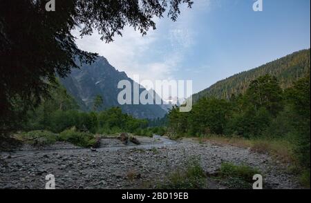 Un ruisseau de montagne ombragé traverse une vallée entre les montagnes couvertes d'arbres. Banque D'Images