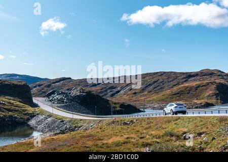 Voiture blanche conduisant la route de montagne de l'autoroute norvégienne le jour ensoleillé de l'automne lumineux. Voyage nature sauvage, ciel bleu, voiture électrique, éco-vie Banque D'Images