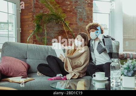 Femme et homme, couple dans des masques de protection et des gants isolés à la maison avec des symptômes respiratoires du coronavirus tels que la fièvre, les maux de tête, la toux. Santé, médecine, quarantaine, concept de traitement. Banque D'Images