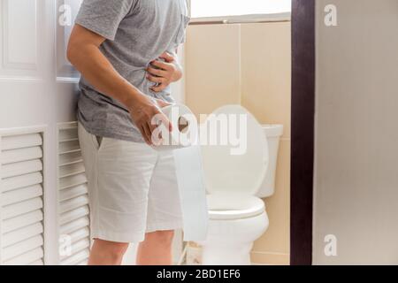 Les hommes qui tiennent le rouleau de toilettes ont le concept de symptôme de coronavirus de douleur abdominale. Banque D'Images