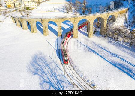 Bernina Express passe sous le viaduc hélicoïdal (spirale) de Brusio, site classé au patrimoine mondial de l'UNESCO, Valposchiavo, Canton de Graubunden, Suisse Banque D'Images