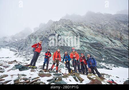 Des alpinistes masculins se tenant sur les rochers et les pierres tout en prenant la rupture de la randonnée dans les montagnes d'hiver. Équipe de randonneurs avec bâtons de randonnée regardant l'appareil photo. Concept de voyage, de randonnée et d'alpinisme. Banque D'Images