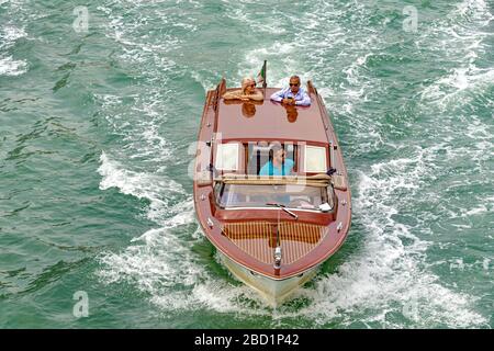 Un bateau-taxi avec deux passagers debout à l'arrière du bateau en regardant la vue, Venise, Italie Banque D'Images