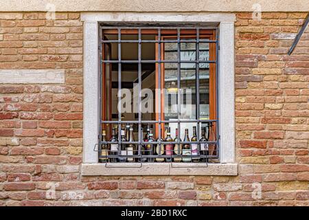 Bouteilles de verre assis sur un seuil de fenêtre derrière la fenêtre barrée en métal dans un mur de brique, Venise, Italie Banque D'Images