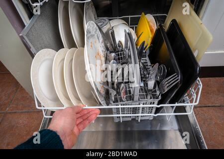 La main d'un homme pousse un portoir chargé de plats dirtys dans un lave-vaisselle. Banque D'Images