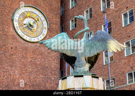 Oslo, Ostlandet / Norvège - 2019/08/30: Sculpture de fontaine de cygne par Dyre VAA devant le bâtiment historique de l'hôtel de ville - Radhuset - avec horloge astronomique Banque D'Images