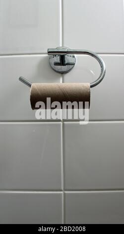 Un rouleau de toilettes vide sur un mur de toilettes en carrelage blanc Banque D'Images