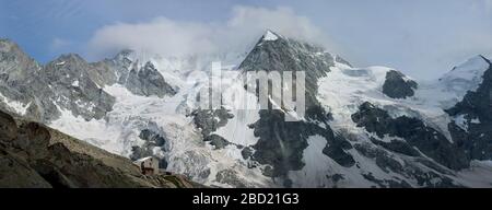 Aperçu panoramique d'une crête de montagnes rocheuses enneigées dans les Alpes suisses, les pics aigus sont dans les nuages de tempête, les pierres grises sont au premier plan Banque D'Images