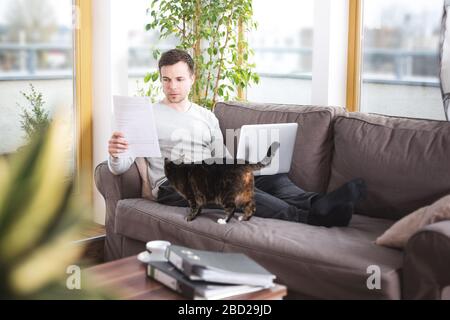 Homme à la maison faisant des documents sur le canapé Banque D'Images