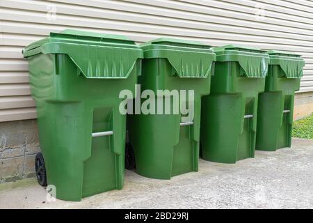 Une piqûre horizontale de quatre poubelles en plastique vert s'aligne contre le mur extérieur d'un condominium. Banque D'Images