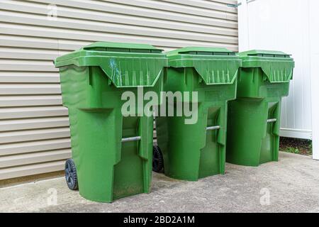 Une piqûre horizontale de trois poubelles en plastique vert s'aligne contre le mur extérieur d'un condominium. Banque D'Images