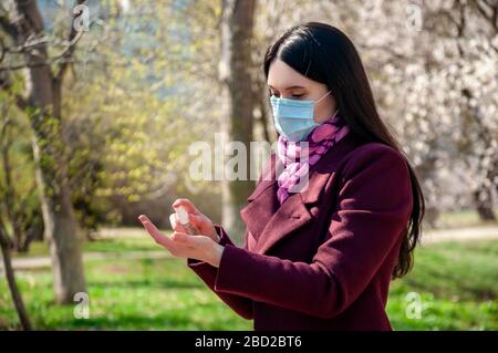 COVID-19. Jeune femme en protection stérile masque médical extérieur désinfecte les mains gel alcoolique antibactérien. Concept de coronavirus. Banque D'Images