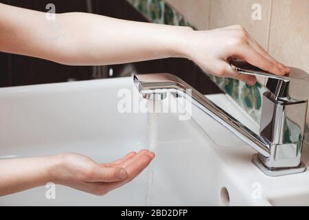 L'enfant ferme l'eau qui coule dans le robinet. Banque D'Images