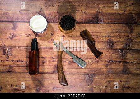 Une sélection de produits pour le toilettage de barbe pour hommes comprenant de l'huile, de la cire et une brosse, tournés sur un fond en bois Banque D'Images