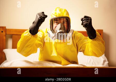 homme auto-isolant dans le lit portant un costume de hazmat et masque se fâchant Banque D'Images