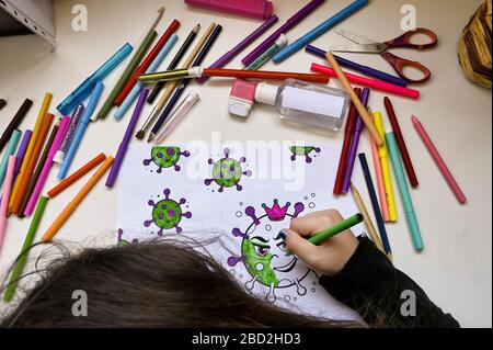 Un enfant colorant la peinture de virus sur une table pleine de couleurs et une bouteille de gel hydroalcoolique Banque D'Images