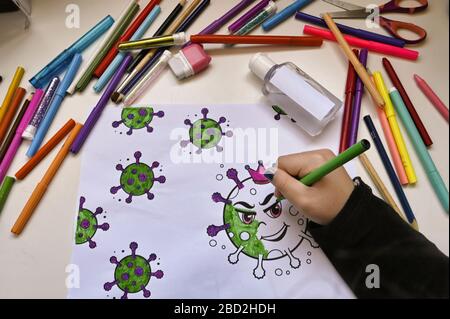 Un enfant colorant la peinture de virus sur une table pleine de couleurs et une bouteille de gel hydroalcoolique Banque D'Images