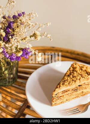 Gros plan sur un gâteau au miel maison avec pruneaux séchés au soleil sur une assiette blanche avec une fourchette d'argent, une table en bois faite à la main, un délicieux café pour le petit déjeuner Banque D'Images