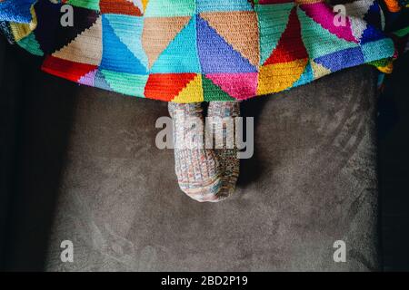 Pieds d'une femme avec chaussettes sur un canapé brun recouvert d'une couverture patchwork Banque D'Images