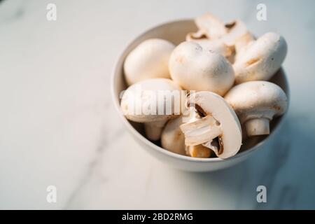 Ensemble de champignons frais entiers et tranchés ​​champignons dans un bol isolé sur fond de pierre blanche. Vue de dessus Banque D'Images