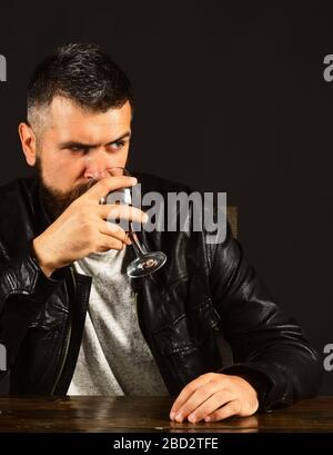 L'homme avec barbe tient un verre de vin sur fond brun foncé. Concept de dégustation et de dégustation. Degustator avec verres de visage occupés wineglass. Le sommelier a un goût de boisson chère Banque D'Images