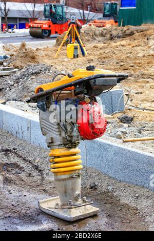 Un rammer vibrant à essence se tient sur un mélange de décombres et de sable sur le fond d'un chantier de construction de routes en blire. Banque D'Images