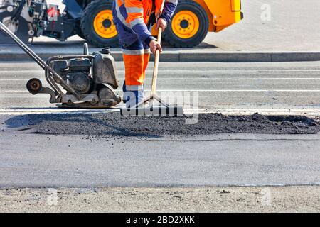 Un travailleur routier répare une partie de la route avec une patinoire, un rammer, un bulldozer et un niveau de bois. Banque D'Images