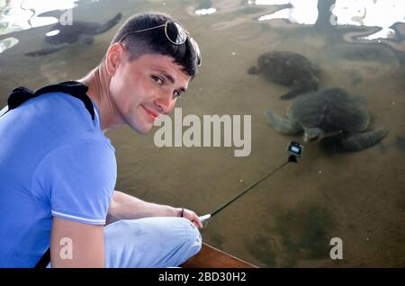 Jeune homme brunette avec appareil photo libère la tortue dans l'eau, le volontaire sauve les tortues, la protection des animaux, le garçon prend des photos de tortue. Sauver les animaux S Banque D'Images